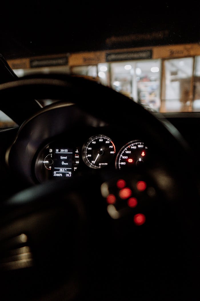 Interior view of a cars illuminated dashboard focusing on the speedometer and steering wheel.