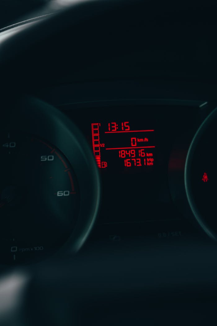 Automobile dashboard displaying time, mileage, and speed metrics in a vivid red light.