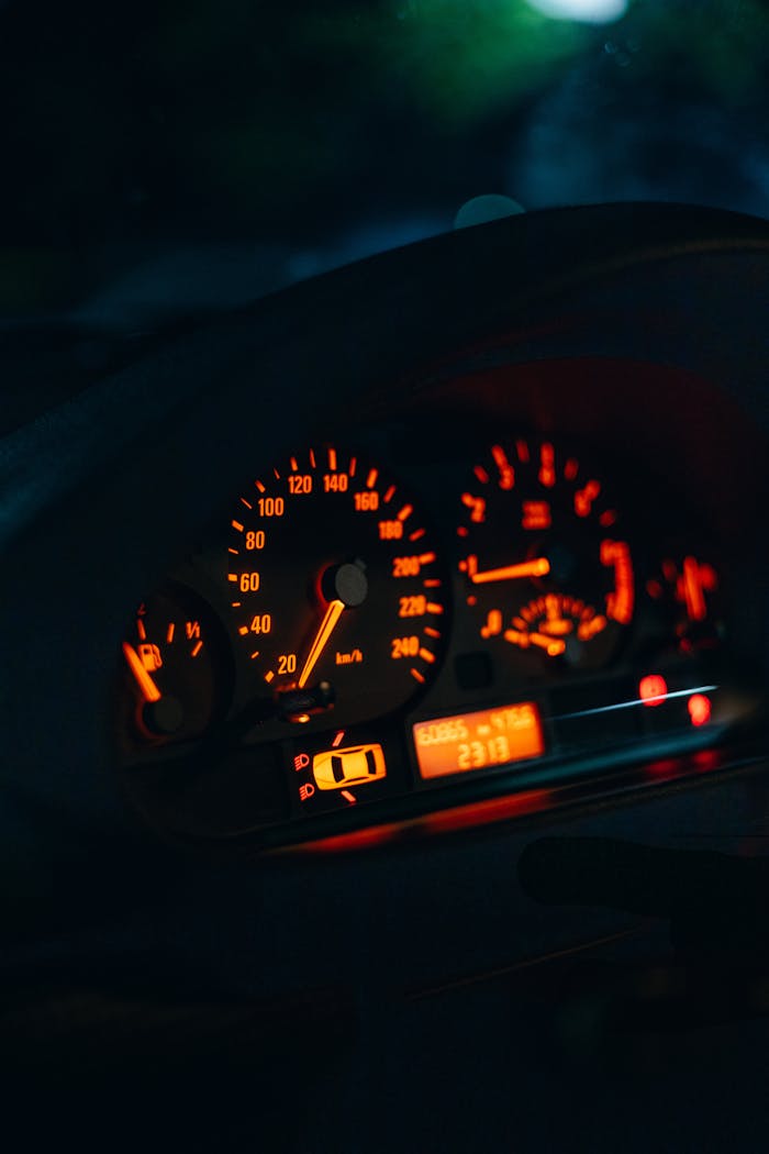 Detailed view of a cars dashboard lights glowing in the dark, focusing on speedometer and fuel gauge.